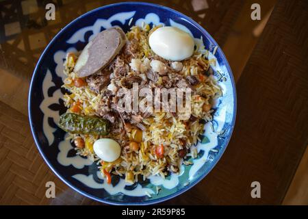 Plaque de pilaf de plov sur fond noir. Cuisine traditionnelle ouzbek. Riz préparé avec des légumes et de la viande. Angle supérieur. Mise au point sélective. Banque D'Images