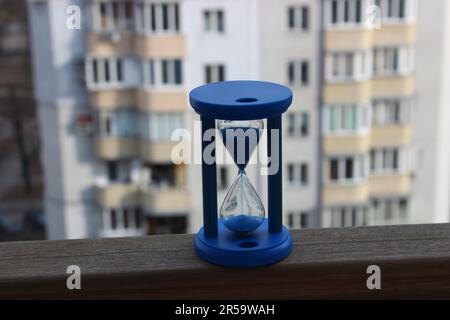 Chute de sable bleu dans un sablier avec des appartements résidentiels floutés sur fond Banque D'Images