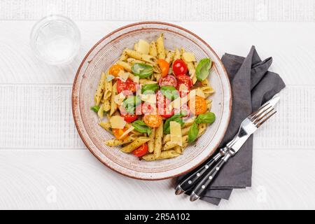 Une délicieuse assiette de pâtes italiennes ornée de tomates fraîches et de feuilles de basilic aromatiques. Pose à plat Banque D'Images