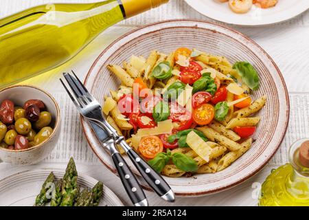 Une délicieuse assiette de pâtes italiennes ornée de tomates fraîches et de feuilles de basilic aromatiques, d'asperges grillées et de crevettes Banque D'Images