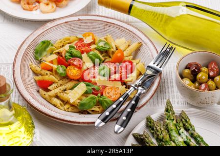 Une délicieuse assiette de pâtes italiennes ornée de tomates fraîches et de feuilles de basilic aromatiques, d'asperges grillées et de crevettes Banque D'Images