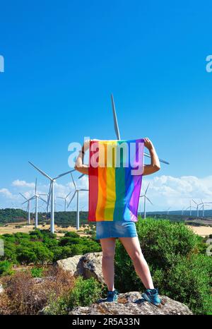 femme avec un drapeau arc-en-ciel comme un cap devant les éoliennes Banque D'Images