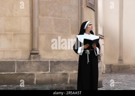 Jeune nun lisant la Bible près de bâtiment à l'extérieur Banque D'Images