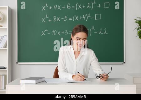 Un jeune professeur de mathématiques donne une leçon à table en classe Banque D'Images