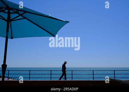 Eastbourne, Royaume-Uni - 11 juillet 2022 : homme marchant sous un parasol bleu sur la plage, en un jour ensoleillé d'été. Protection solaire. Concept de voyage et de vacances. Banque D'Images