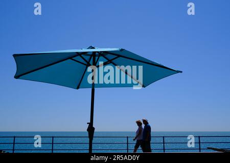 Eastbourne, Royaume-Uni - 11 juillet 2022: Couple marchant sous un parasol bleu sur la plage dans une journée ensoleillée de l'été. Protection solaire. Voyages et vacances concep Banque D'Images