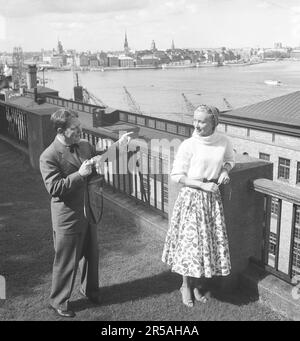 Photographe amateur en 1950s. Un couple de touristes à Stockholm et l'homme se tient avec son appareil photo et veut immortaliser son partenaire avec le ruisseau de Stockholm en arrière-plan. Elle est vêtue d'une jupe d'époque et d'un pull tricoté. Il est l'acteur américain Burgess Meredith qui prend une photo de sa femme suédoise Kaja Sundsten. Suède 1954. Photo Kristoffersson Réf. BF78-1 Banque D'Images