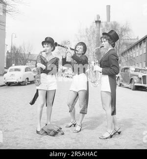 Trois femmes vêtues de manteaux de grenouille et de culottes blanches et de chapeaux hauts sont debout et jouent des instruments de vent. Deux d'entre eux jouent le saxophone et la femme au milieu joue la clarinette. Un manteau de grenouille est un costume de fête pour les hommes qui est utilisé, par exemple, pour les mariages. Il n'est pas considéré acceptable pour les femmes de porter des manteaux sauf lors des soirées d'habillage. Suède 1956. Kristoffersson réf. BX2-5 Banque D'Images