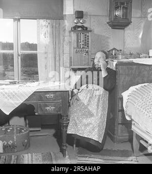 Une femme âgée dans la zone peu peuplée de Norrbotten à la maison, près du tableau de commutation téléphonique fixé au mur. Il était courant dans les villages des zones peu peuplées que quelqu'un avait le standard téléphonique à la maison et était responsable de la connexion des appels téléphoniques de et vers les résidents du village. Vous pouvez également y aller et appeler si vous n'avez pas de téléphone. Suède 1949. Kristoffersson réf. AS75-4 Banque D'Images