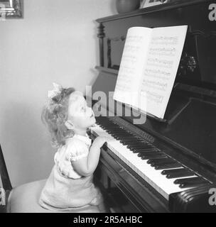 Faire de la musique. Une petite fille est assise devant le piano et tient ses mains et ses doigts sur les touches du piano comme si jouer, regardant la feuille de musique devant elle. Suède 1946. Kristoffersson réf. Y106-1 Banque D'Images