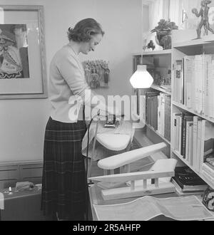 Repassage dans le 1950s. Une femme a vu repasser ses vêtements à la maison. Peut-être avant un voyage de vacances comme sa valise est vue debout sur le sol à côté d'elle. Elle est Mme Blomberg résidant à Lidingö Stockholm. Suède mars 1956 Banque D'Images
