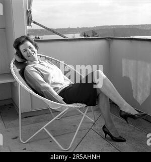 Décoration de la maison du 1960s. Une femme est assise confortablement dans la chaise de pont de 1950s 1960s conçu avec des tuyaux en acier avec un centre rond et quatre jambes. Le siège est en cuir. Un design populaire à l'époque avec de nombreuses variétés différentes, certaines plus connues que d'autres. Elle est actrice Sickan Carlsson 1915-2011 dans à la maison sur le balcon. Suède 1964 Banque D'Images