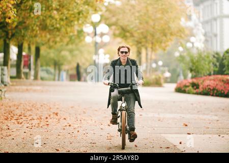 Portrait en plein air d'un beau homme à cheveux lus qui fait du vélo dans une ville Banque D'Images