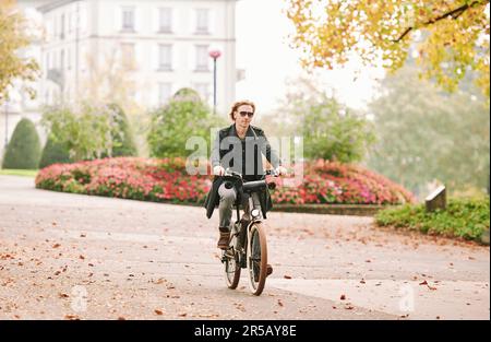 Portrait en plein air d'un beau homme à cheveux lus qui fait du vélo dans une ville Banque D'Images