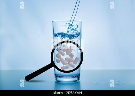 Une loupe avec de grandes tablettes blanches devant une vitre d'eau. Concept: Antibiotiques dans l'eau potable Banque D'Images