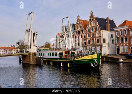 Haarlem, pays-Bas - 11 avril 2022: Barge passant sous le pont-plan surélevé Gravestenen sur la rivière Spaarne avec maisons à pignon en arrière-plan. Banque D'Images