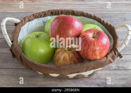 Un panier de pommes fraîchement cueillies sur une table rustique en bois, avec une poignée blanche pour faciliter le transport Banque D'Images