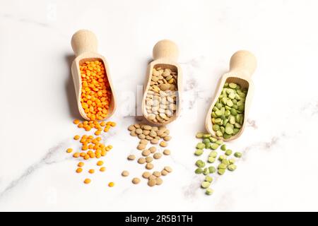 Lentilles rouges, vertes et brunes dans une cuillère en bois et sur un comptoir de cuisine en marbre blanc avec espace pour les copies Banque D'Images
