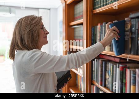 Femme âgée plaçant des livres sur une étagère pleine de livres à l'intérieur de sa maison. Banque D'Images