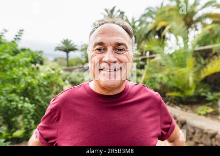 Joyeux homme âgé souriant dans la caméra tout en faisant des activités sportives dans un parc public Banque D'Images