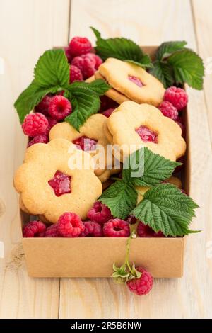 Biscuits faits maison avec confiture de framboises et framboises fraîches dans une boîte artisanale sur fond de bois. Banque D'Images