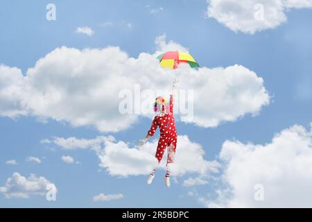 Clown drôle tenant un parapluie et volant dans le ciel Banque D'Images