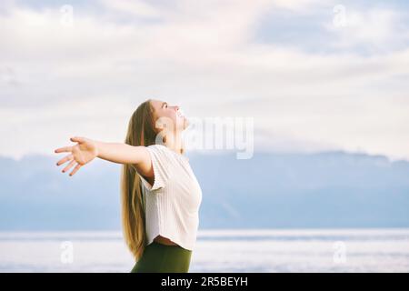 Portrait extérieur de la belle jeune femme appréciant une belle journée ensoleillée au bord du lac de montagne, bras larges ouverts, respirer l'air frais alpin Banque D'Images