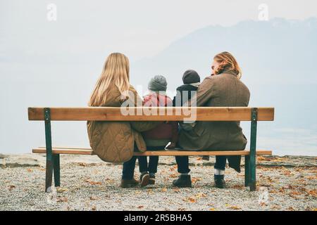 Famille de 4 personnes assises sur banc, appréciant la belle journée d'automne au bord du lac, temps froid, vue arrière Banque D'Images