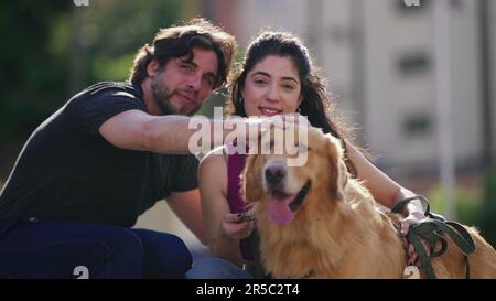 Couple posant pour une photo avec leur Golden Retriever PET aimé dans un cadre extérieur. Moment sincère de l'homme et de la femme caressant affectueusement leur ca Banque D'Images