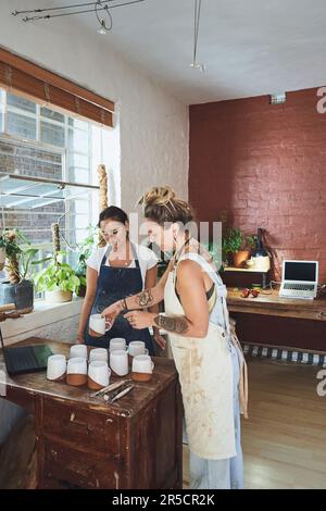 Aujourd'hui, nous apprenons, demain, nous gagnons. deux jeunes femmes qui font des mugs dans un studio de poterie. Banque D'Images