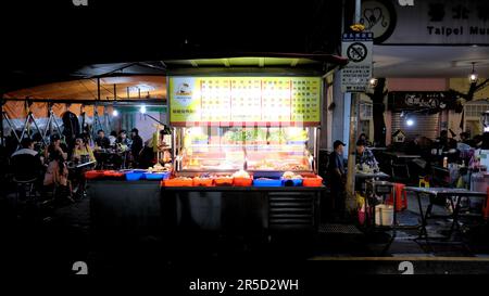 Stand de nourriture de rue au marché de nuit touristique de Huaxi Street à Taipei, Taiwan; tables et clients de salle à manger assis en arrière-plan. Banque D'Images