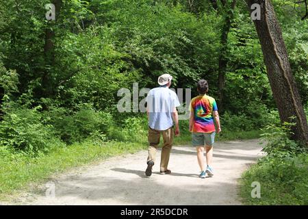 Femme en chemise teinte au noeud marchant avec un homme portant un chapeau souple sur le sentier de la rivière des Plaines à Camp Ground Road Woods à des Plaines, Illinois Banque D'Images