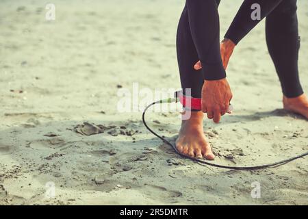 Messagerie instantanée associée au surf. un surfeur nouant sa laisse de planche de surf autour de sa cheville. Banque D'Images