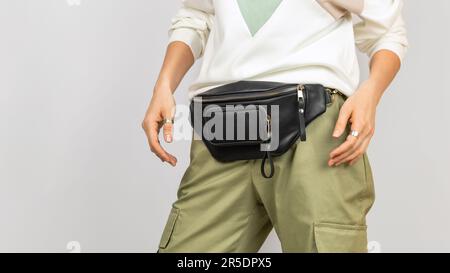 Sac de taille en cuir noir sur une femme portant un pantalon vert et un sweat-shirt. Articles d'accessoires en cuir faits main Banque D'Images