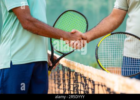 Gros plan sur le concept de divertissement des amis indiens senior saluant leurs proches en serrant la main avant de jouer au match de tennis sur le court Banque D'Images