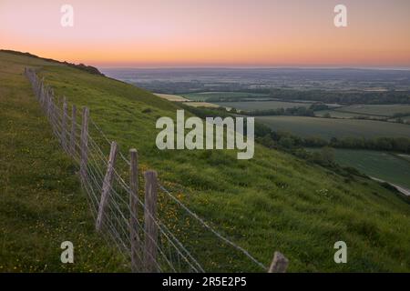 Vue panoramique depuis Butts Brow sur le parc national de South Downs au coucher du soleil, avec des collines ondulantes, des champs patchwork et une clôture menant à l'horizon. Banque D'Images