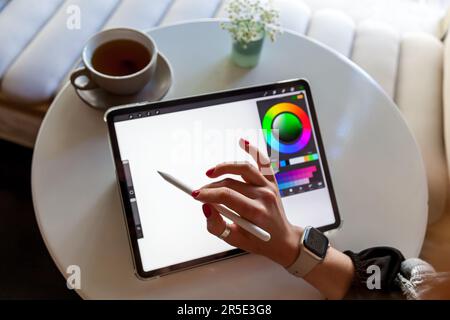Une fille dans un café tire avec un stylet sur une tablette graphique.travail à distance d'un concepteur, d'un visualiseur ou d'un artiste Banque D'Images