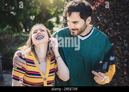 Un cliché spontané d'un jeune homme et d'une jeune femme qui marchent dans le parc un jour ensoleillé, redonnant le 90s avec un magnétophone à cassette. Ils partagent une paire d'écouteurs Banque D'Images