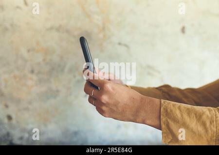 Voyons ce qui se passe sur les amis. Gros plan d'une femme méconnaissable utilisant un téléphone portable contre un mur. Banque D'Images