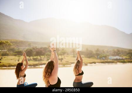 Le yoga vous donne les moyens de développer la patience. trois jeunes femmes pratiquant le yoga sur la plage. Banque D'Images