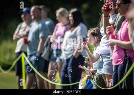 Un enfant soufflait de bulles tout en regardant le football de la base avec des spectateurs par beau temps. Banque D'Images