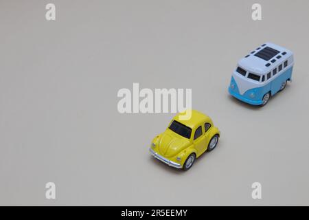 Une fourgonnette bleu et blanc suit un coléoptère jaune sur fond gris, partant du coin supérieur droit. Copier l'espace. Concept de style de vie minimal. Banque D'Images