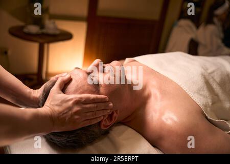 Masseuse qualifiée donnant un massage de la tête à l'homme adulte Banque D'Images