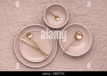 Jeu de plaques rondes beige de différentes tailles sur table, vue de dessus. Couverts dorés et ustensiles de service. Une vaisselle vide sur un tissu beige clair tablec Banque D'Images