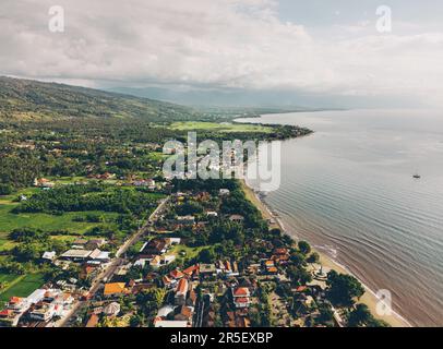 Une jolie ville tropicale se trouve au bord de l'océan, entourée d'arbres et de collines. La scène paisible a un ciel bleu, des nuages moelleux, et l'eau chatoyante Banque D'Images