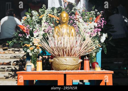 Statue de Bouddha d'or miniature décorée de fleurs colorées pendant le Saint-Vesak. Banque D'Images