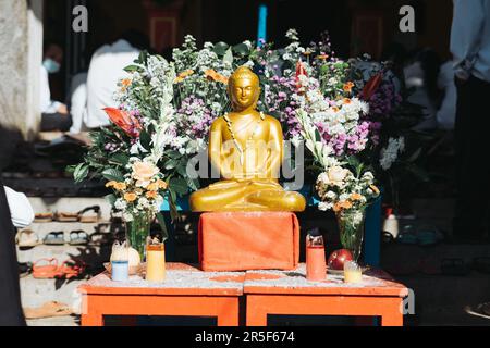 Statue de Bouddha d'or miniature décorée de fleurs colorées pendant le Saint-Vesak. Banque D'Images
