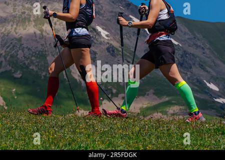 deux femmes sentier de marche sur prairie verte en arrière-plan montagne, chaussettes de compression sur ses pieds et bâtons de randonnée dans les mains Banque D'Images