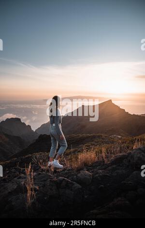 Jeune femme avec une tenue urbaine regardant un beau coucher de soleil depuis le sommet de Teno sur l'île des canaries de Ténérife pendant ses vacances touristiques Banque D'Images