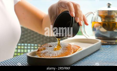 Une femme verse du sirop d'érable sur des crêpes au petit déjeuner Banque D'Images